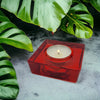 Small square glass tealight holder in translucent red with a lit white tea light candle inside