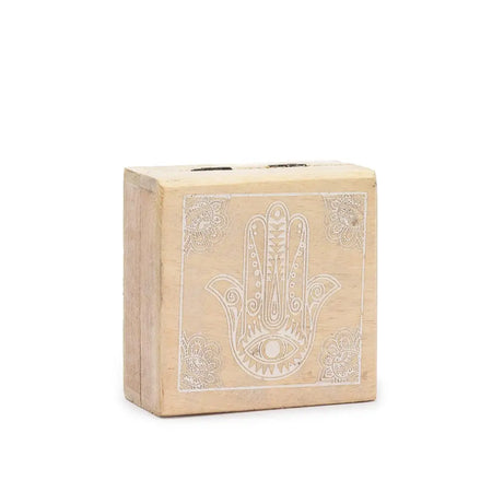 A small square wooden box in whitewash featuring an intricately engraved hamsa hand with a central eye motif