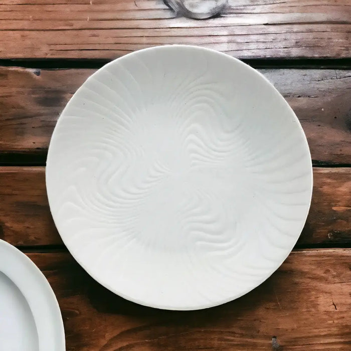 Small white porcelain plate with a subtle swirling textured pattern radiating from the center