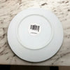 Small white porcelain plate with swirl pattern and a barcode sticker in the center on a white background
