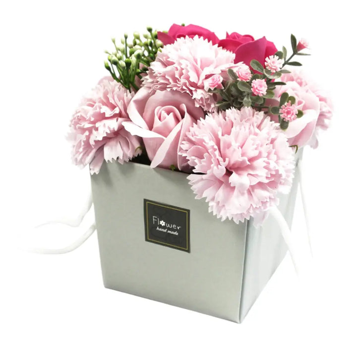 A soap flower bouquet with pink and deep rose soap carnations and roses in a light gray square box with greenery