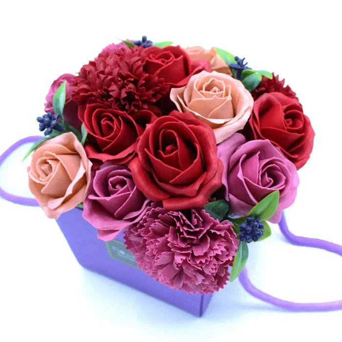 A soap flower bouquet with red pink and peach handcrafted soap flowers inside a purple gift box
