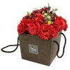 A soap flowers bouquet with red roses and carnations in a brown paper gift box with black handles