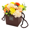 A soap flower bouquet with yellow orange and cream artificial soap flowers arranged in a brown gift box with handles