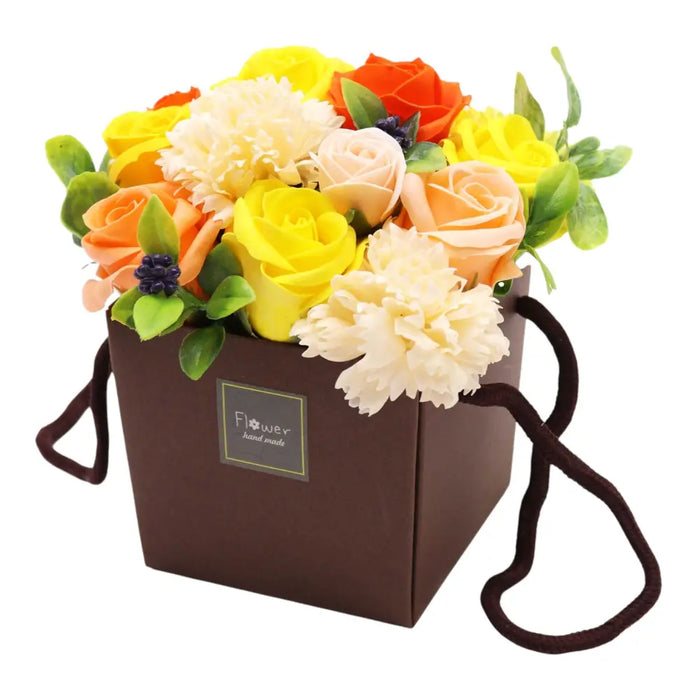 A soap flower bouquet with yellow orange and cream artificial soap flowers arranged in a brown gift box with handles