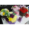 A soap flower bouquet with yellow roses white carnations and purple chrysanthemums in a purple box with green leaves