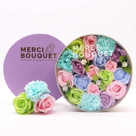 A pastel soap flower gift box with pink, blue, green, and lavender soap flowers in a round purple container
