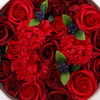 A soap flower gift box with red roses and carnations made from resin featuring glossy leaves and dark purple accents