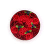 A circular soap flower gift box with vibrant red roses and carnations accented by green leaves and small purple flowers