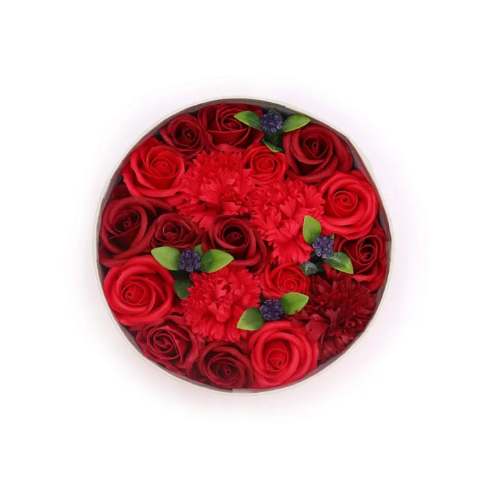 A circular soap flower gift box with vibrant red roses and carnations accented by green leaves and small purple flowers