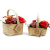 Two woven wicker baskets each hold soap flowers in red and white with green leaves in a medium size arrangement