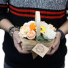 A woven wicker basket filled with peach orange white and yellow soap flowers in a medium red basket