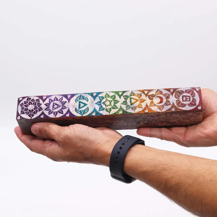 A rectangular wooden soapstone incense box with seven colorful chakra symbols on its polished surface