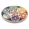 A soapstone incense holder disc with seven colorful chakra symbols hand carved on a light beige stone coaster