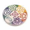 A circular soapstone incense holder with hand carved colorful seven chakra symbols on a light wooden coaster