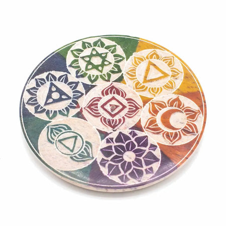 A circular soapstone incense holder with hand carved colorful seven chakra symbols on a light wooden coaster