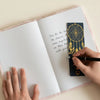 A navy blue soft book dream journal with 80 pages and a gold dreamcatcher bookmark with dangling feathers