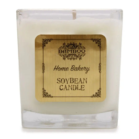 A white soy wax candle in a clear 5cm square glass jar with a gold bamboo home bakery label
