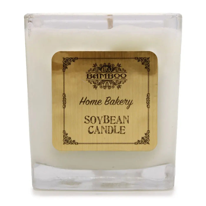 A white soy wax candle in a clear 5cm square glass jar with a gold bamboo home bakery label