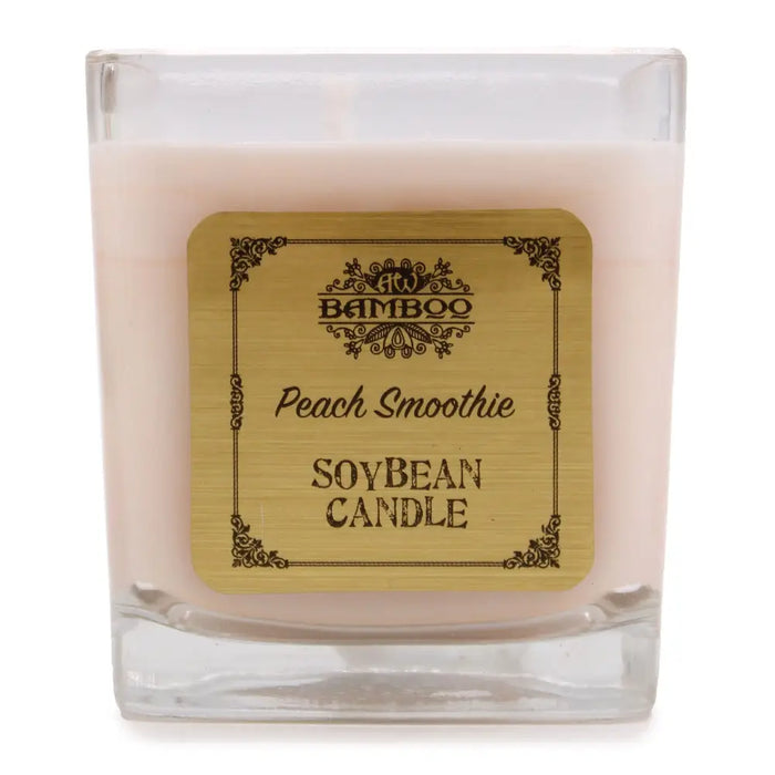 A square glass soy wax jar candle in soft pink with an ornate gold peach smoothie label by bamboo, 5cm wide