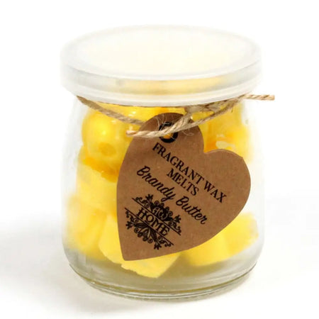 A clear glass jar of yellow brandy butter soy wax melts sealed with a transparent lid and brown heart tag tied by twine