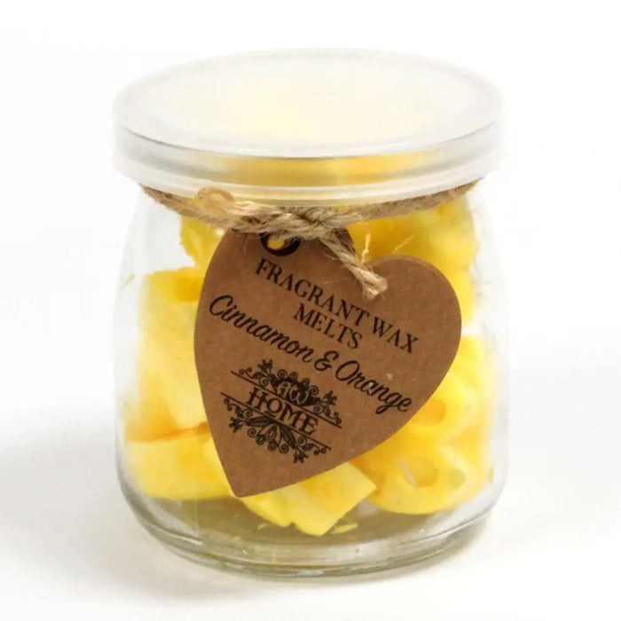 A clear glass jar of yellow cinnamon and orange soy wax melts sealed with a lid and a brown heart tag tied with twine