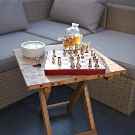 Red wooden chess set with metallic pieces on a checkered board on a square folding coffee table made of teak wood