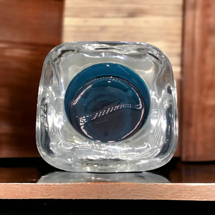 Clear glass tealight holder with square rounded base and deep teal circular interior in glass tealight design