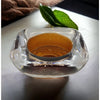A clear square-shaped glass tealight holder with amber liquid and a smooth reflective surface in two-tone design
