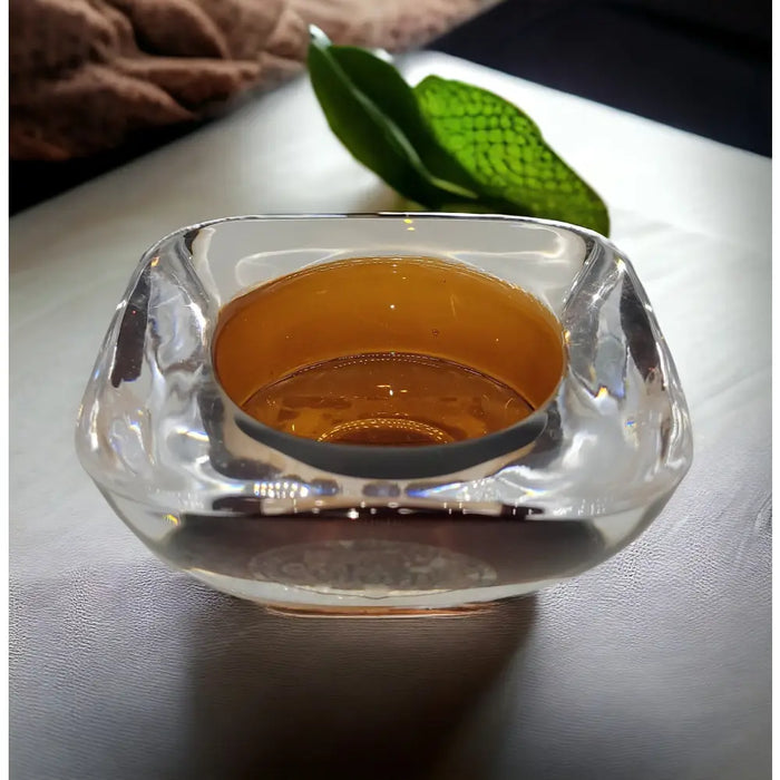 A clear square-shaped glass tealight holder with amber liquid and a smooth reflective surface in two-tone design