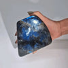 A hand holds a smooth polished madagascar labradorite stone with blue and silver iridescent patterns weighing about 900 grams