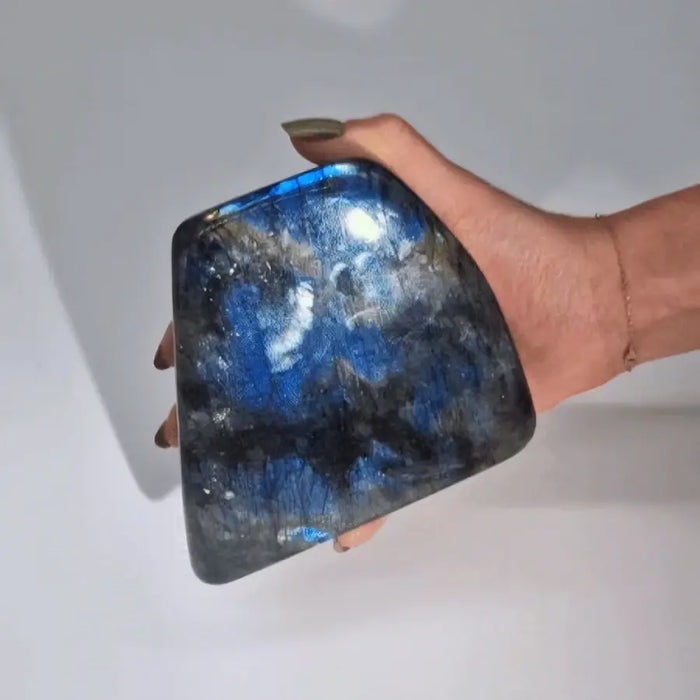 A hand holds a smooth polished madagascar labradorite stone with blue and silver iridescent patterns weighing about 900 grams