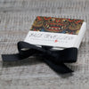 A white jewelry box with a balinese mask design in reds and golds tied with black ribbon for sterling silver and 18ct yellow gold earrings