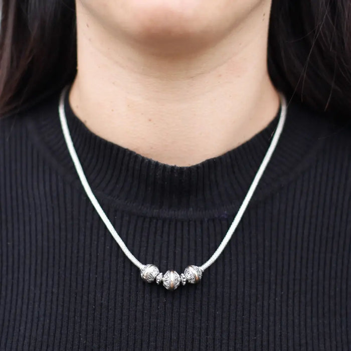 Sterling silver necklace with three charm beads and two spacers on a white cord featuring 18ct yellow gold accents