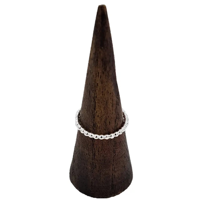 A sterling silver stackable ring with a beaded design sits on a dark wooden cone display
