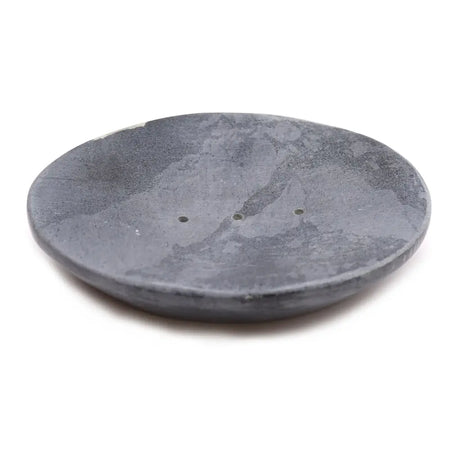 Gray soap dish made of soapstone with a classic oval shape and three small drainage holes and a smooth texture
