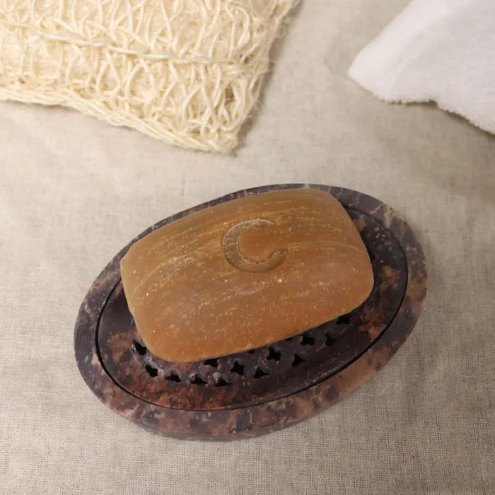 A warm amber soap with a crescent moon rests on a dark brown marbled stone soap dish with cut-out patterns