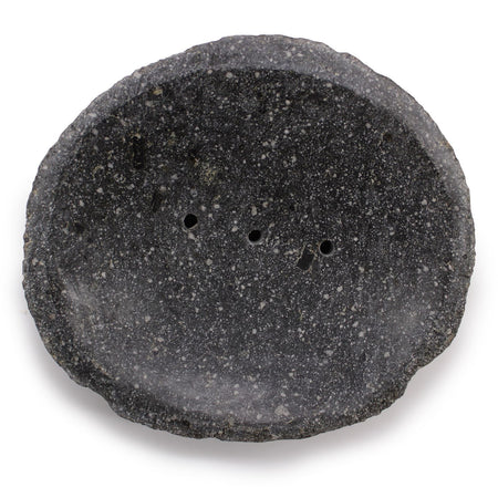 A dark gray speckled stone soap dish with rough natural edges and three small drainage holes for bathroom use