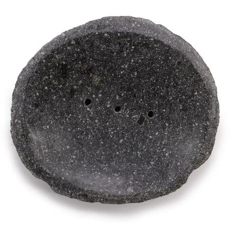 A dark gray speckled stone soap dish with rough natural edges and three small drainage holes for bathroom use