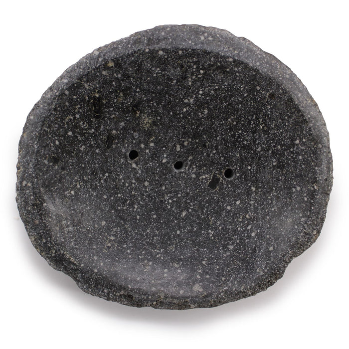 A dark gray speckled stone soap dish with rough natural edges and three small drainage holes for bathroom use