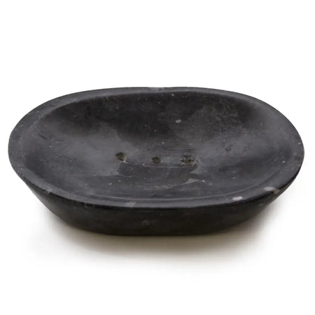 Black marble soap dish in an oval shape made of matte stone with a slightly uneven surface and drainage holes