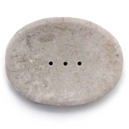 A smooth oval soap dish made of cream marble with three small drainage holes for bathroom use