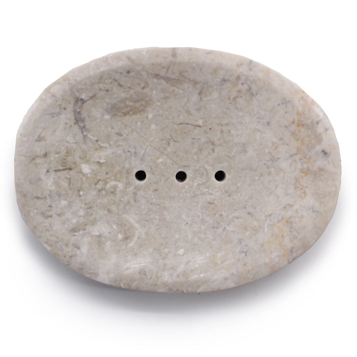A smooth oval soap dish made of cream marble with three small drainage holes for bathroom use