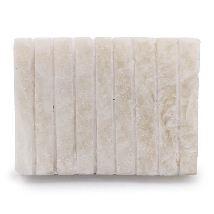 Stone soap dish in white onyx with vertical grooves and subtle natural veining on an off-white rectangular tile