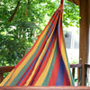 A vibrant striped hammock with red yellow green and blue cotton hanging outdoors between trees