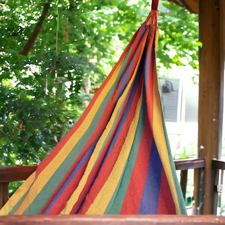 A vibrant striped hammock with red yellow green and blue cotton hanging outdoors between trees