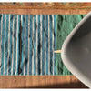 A handwoven indian cotton rug with vertical teal white and green stripes in a cozy indoor setting
