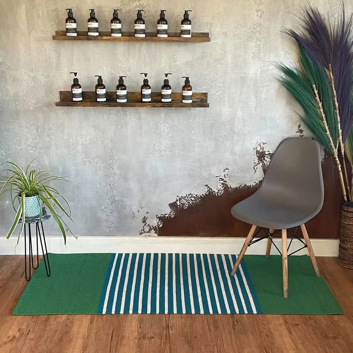 Gray molded plastic chair with wooden legs next to a striped blue green indian cotton rug in a living space