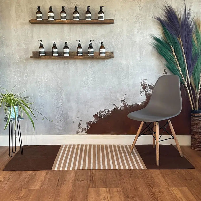 Gray molded plastic eames chair with wooden legs beside a dark brown beige striped indian cotton rug on wooden floor