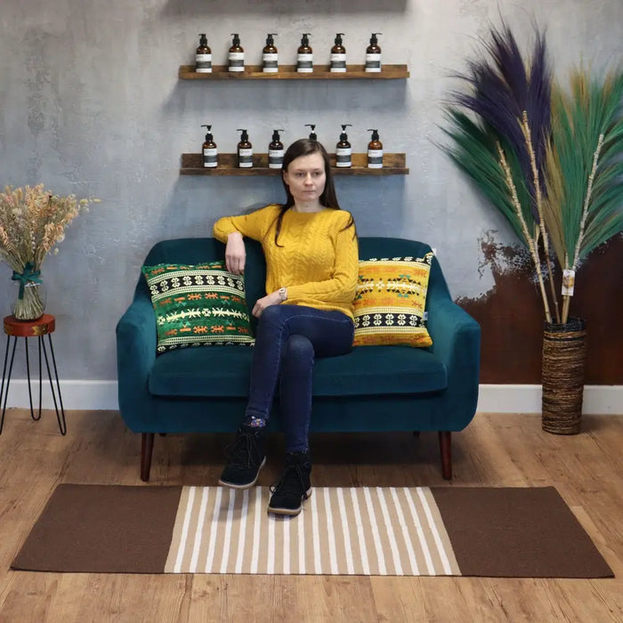 Teal velvet sofa with wooden legs and patterned pillows on a striped indian cotton rug in dark brown and beige